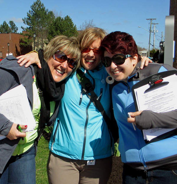 Photo shows Josee, Dominique and Denise with arms around each other, laughing and smiling at the camera.  Two of them are holding clipboards.